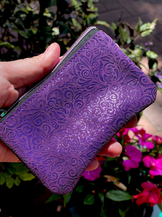 Purple textured wallet held by a hand with a blurred floral background