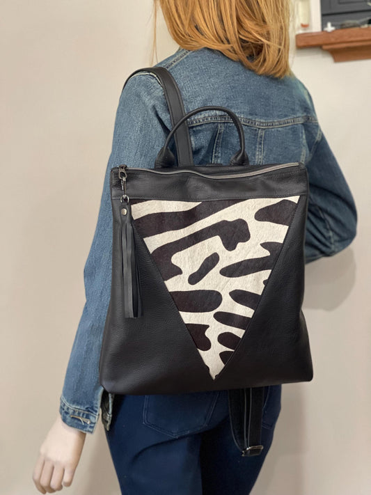 Person wearing a black and zebra print on cowhide backpack with tassel and using 1 strap as a shoulder bag