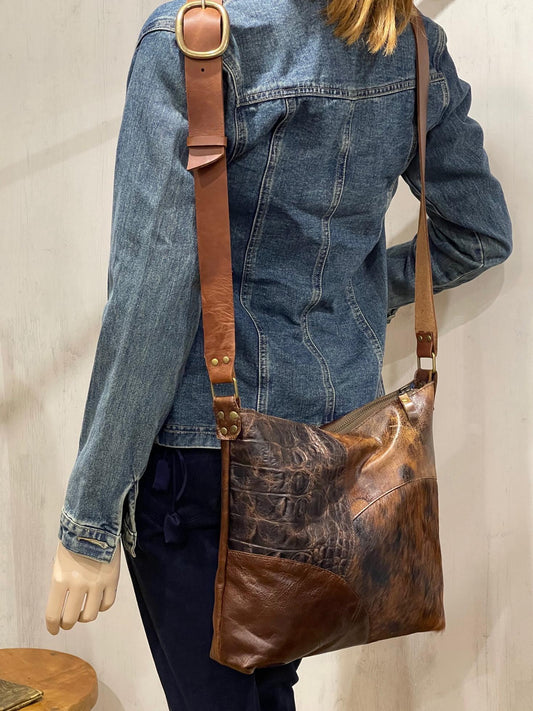 Person wearing a denim jacket with a combination brown leather shoulder bag.