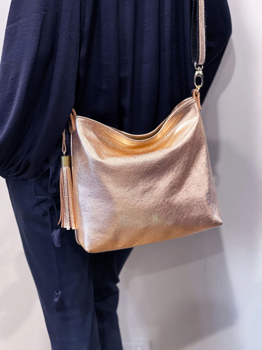 Person wearing a metallic rose peach gold handbag across body for hands free, against a neutral background