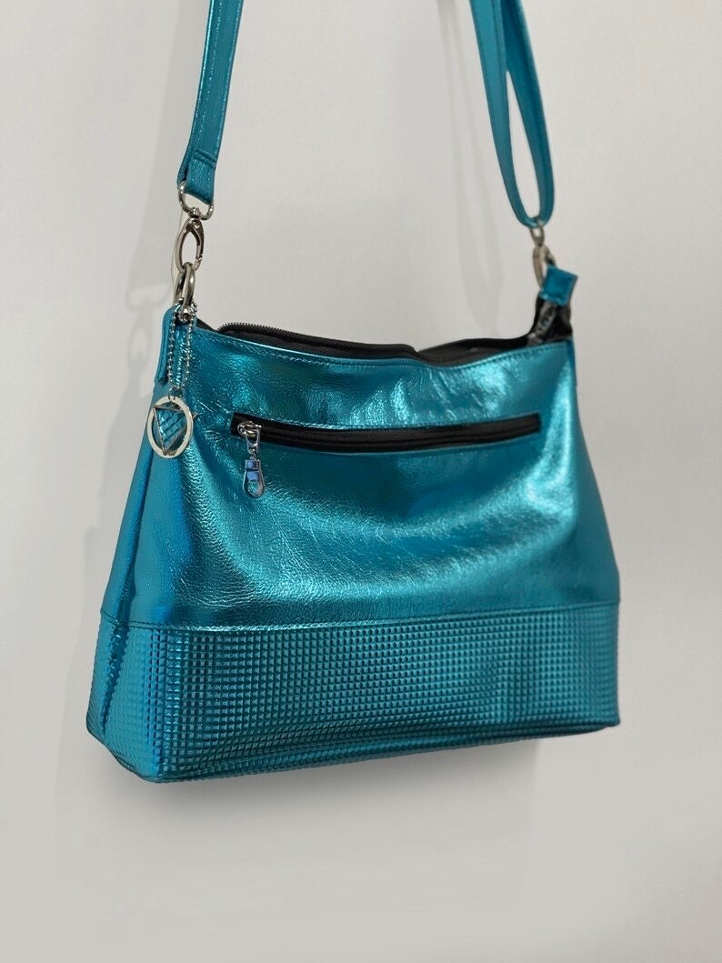 turquoise metallic leather bag with textured surface and visible stitching with removable turquoise strap adjustable for length, and a outside zipper pocket