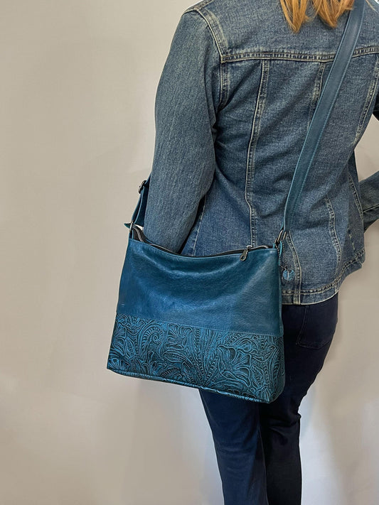 Person wearing a blue denim jacket and carrying a matching Teal blue handbag with tooled garden design.
