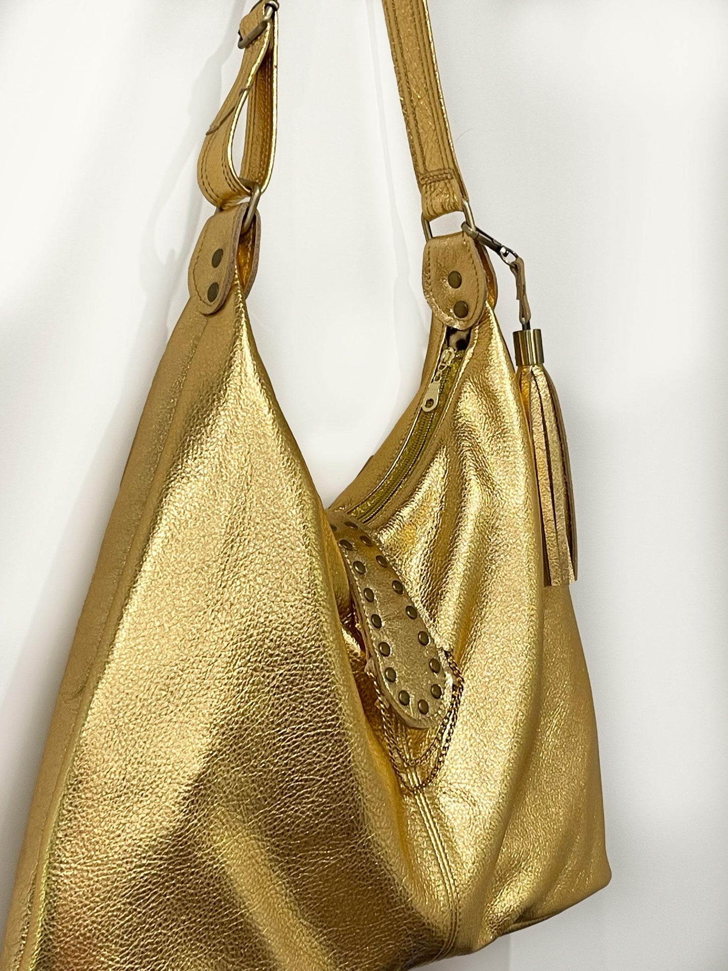 Gold leather handbag with studded detail on a white background. top gold zipper