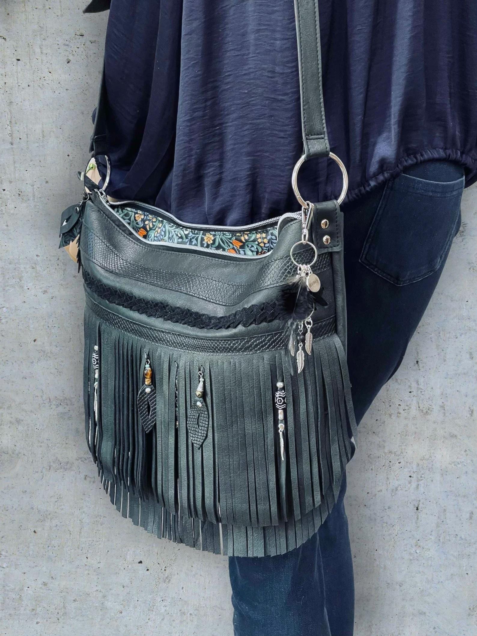 black fringe handbag with decorative elements worn by a person against a neutral background