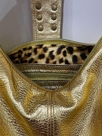 metallic Gold handbag with leopard print interior on a light gray background. inside zipper pocket