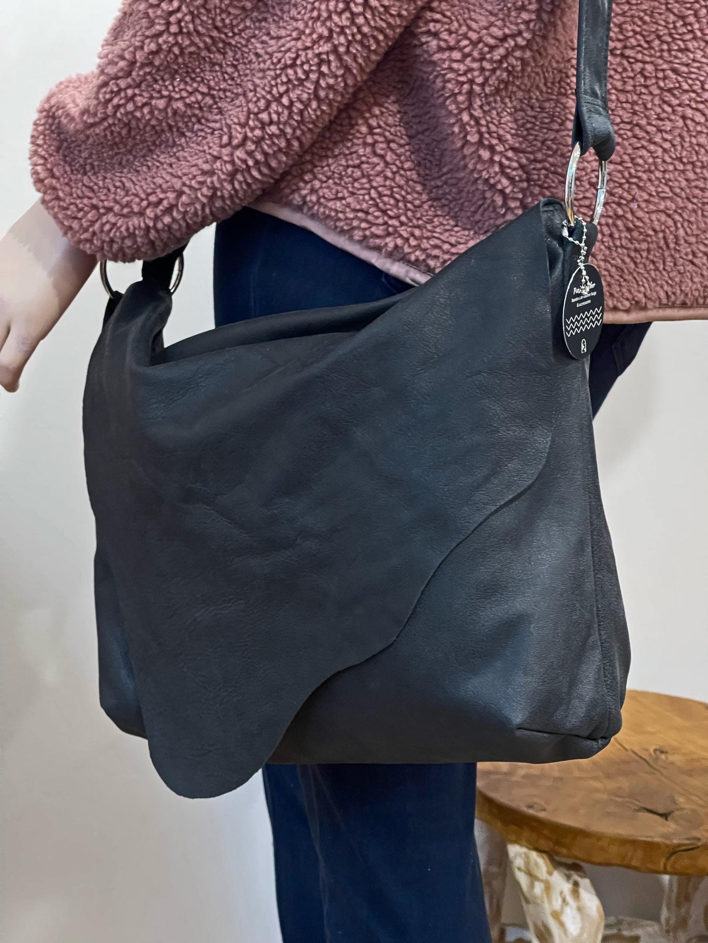 Person holding a black handbag with a natural edged flap closure