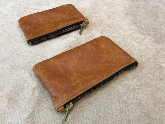 Two brown leather zippered pouches on a beige fabric background