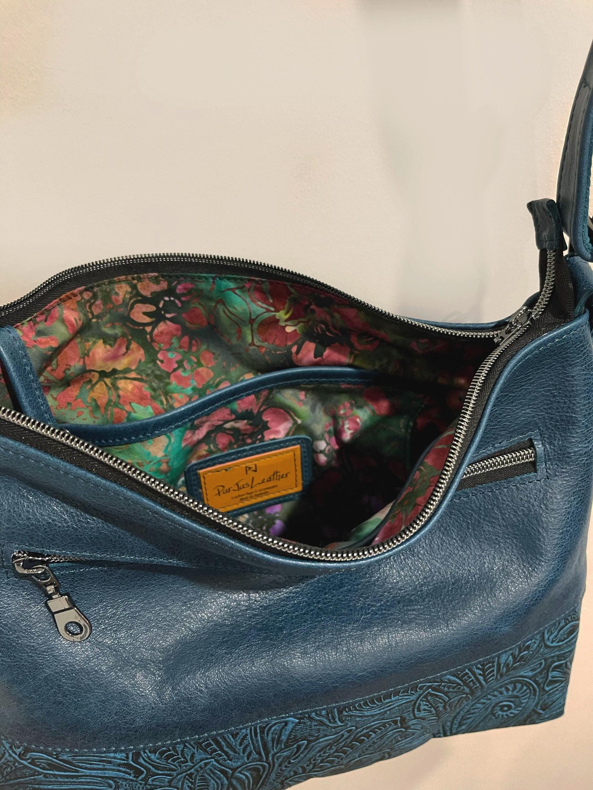 Deep teal Blue leather handbag with batik jewel interior lining on a beige background