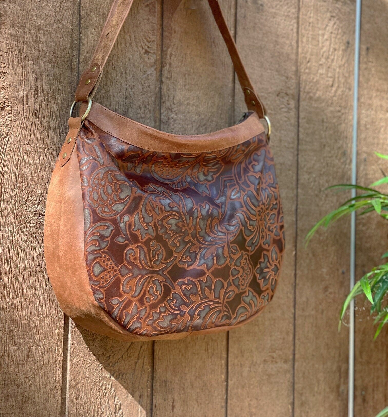Brown and tan leather handbag with intricate patterns hanging on a wooden wall.