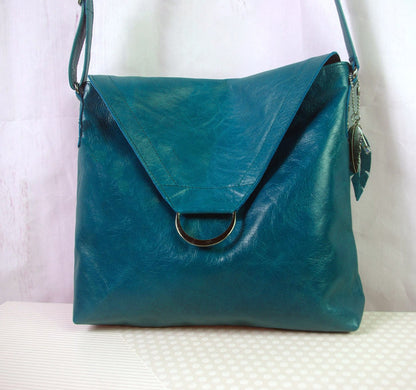 Teal leather handbag with a silver clasp on a white surface. flap with magnet closure