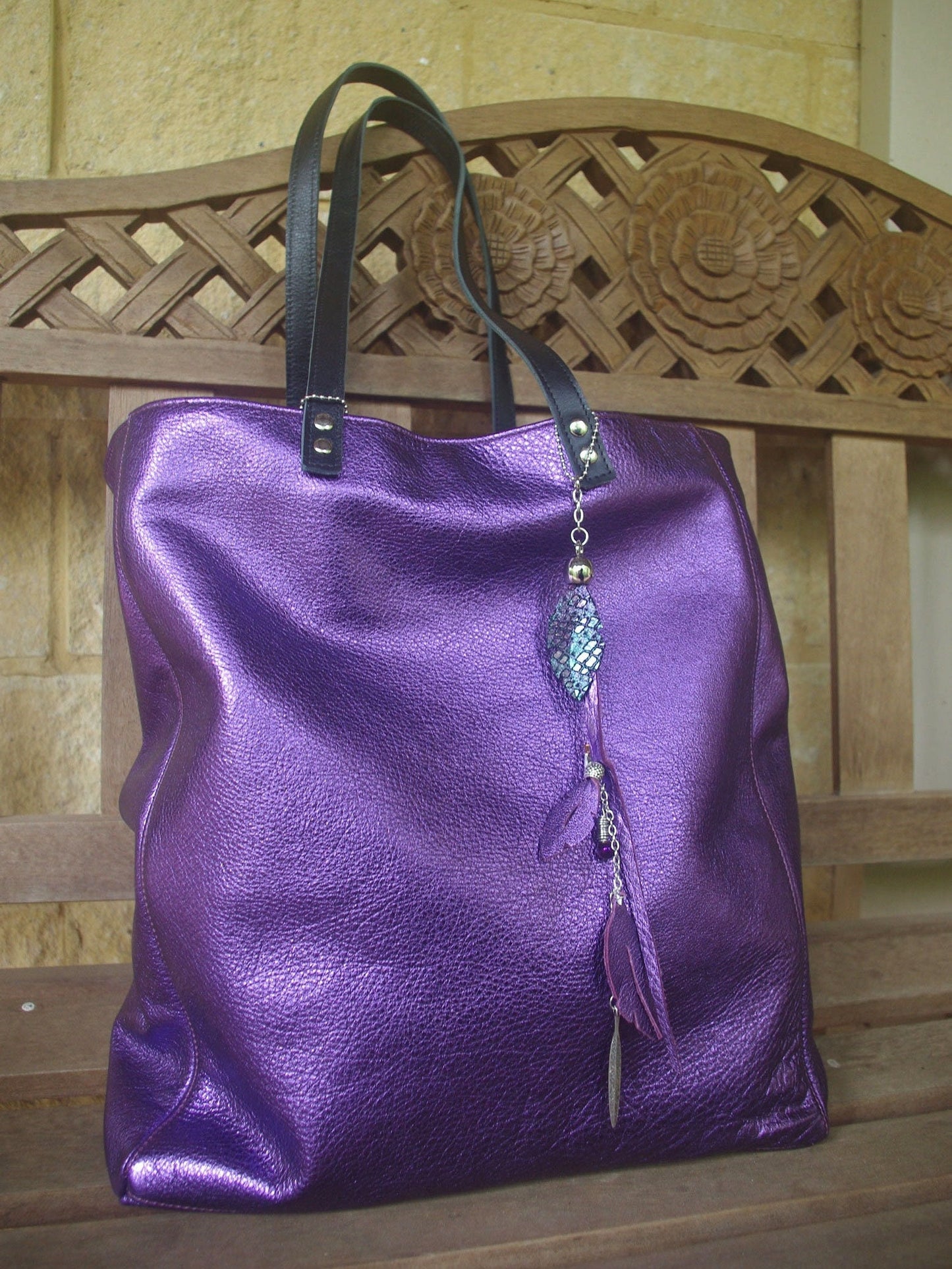Purple handbag with a decorative charm on a wooden bench. silver hardware