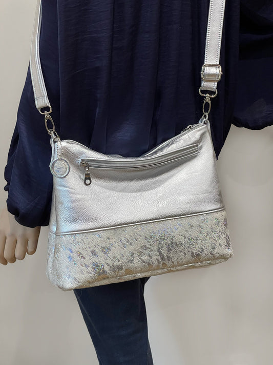 Silver handbag with a white holographic cowhide bottom section worn by a person against a neutral background