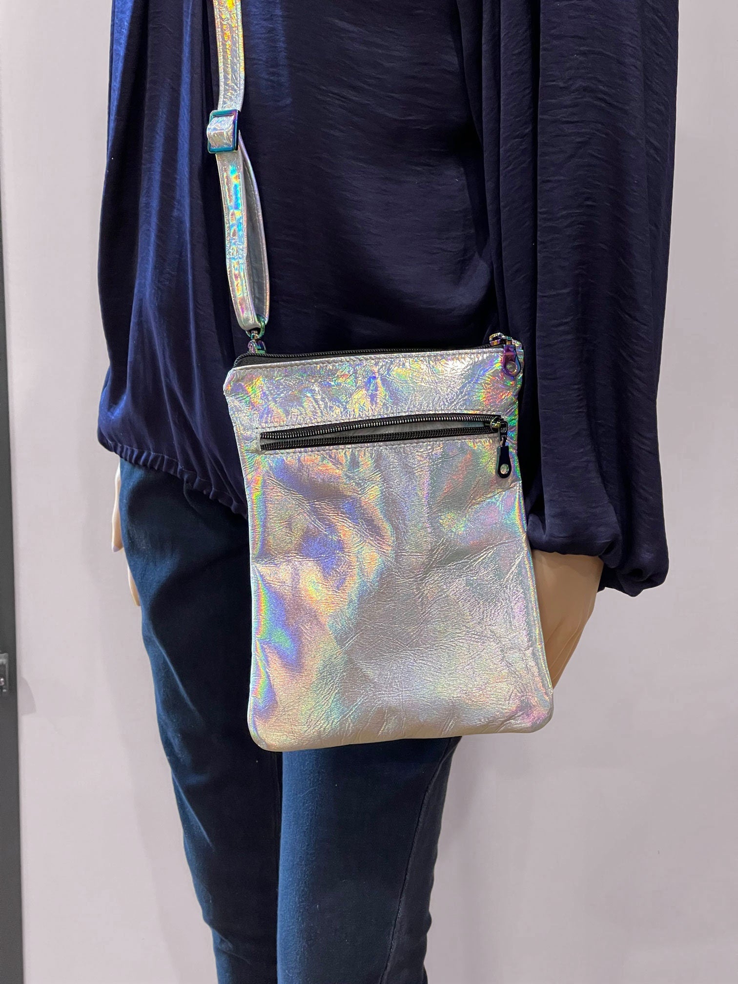 Person wearing a holographic silver crossbody bag with easy access outside zipper pocket