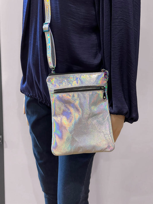 Person wearing a holographic silver crossbody bag with easy access outside zipper pocket