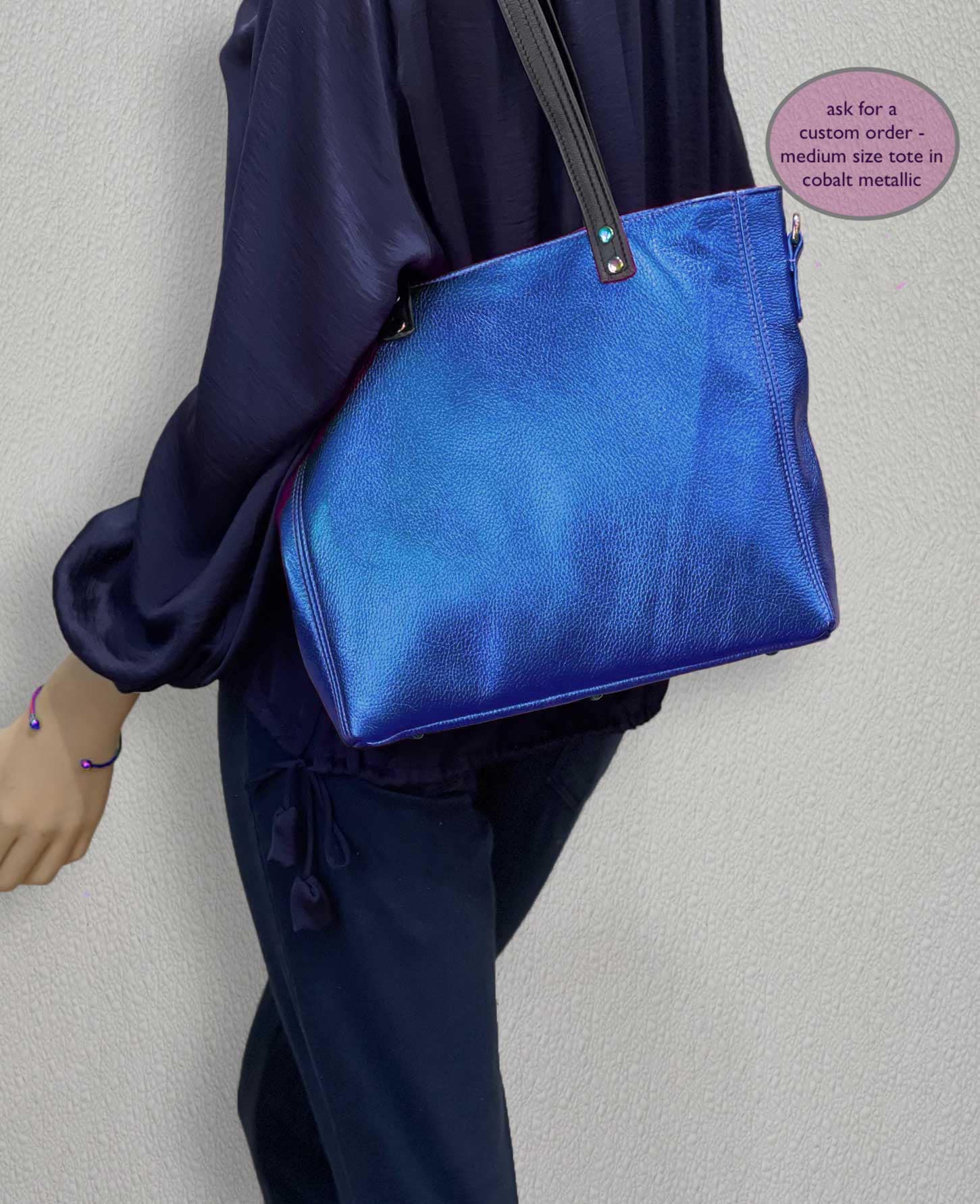 Person wearing a cobalt blue metallic handbag against a plain background