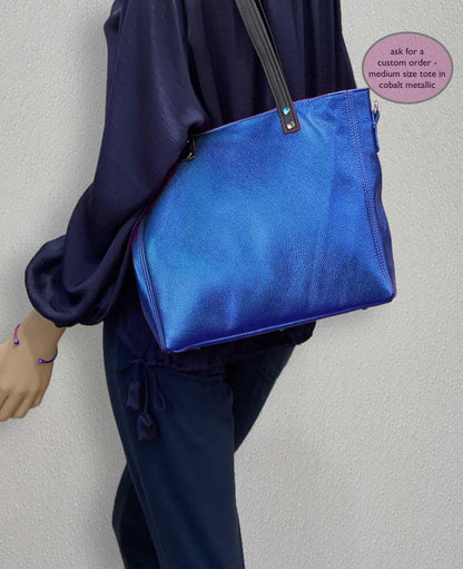 Person wearing a cobalt blue metallic handbag against a plain background