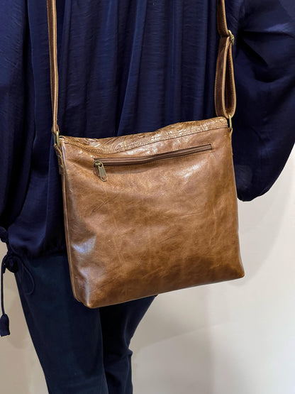 acorn Brown leather crossbody with zipper pocket outside worn by a person against a neutral background