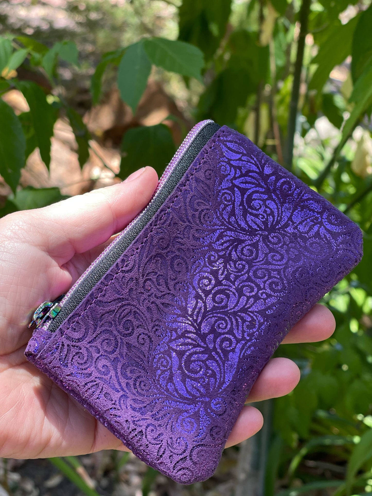 Purple embossed wallet held in a hand with a green leafy background