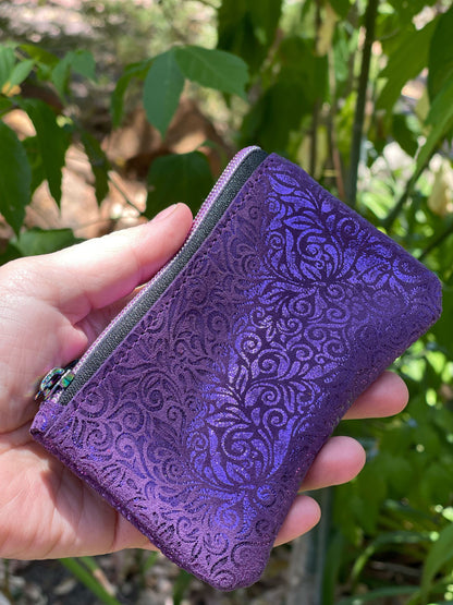 Purple embossed wallet held in a hand with a green leafy background