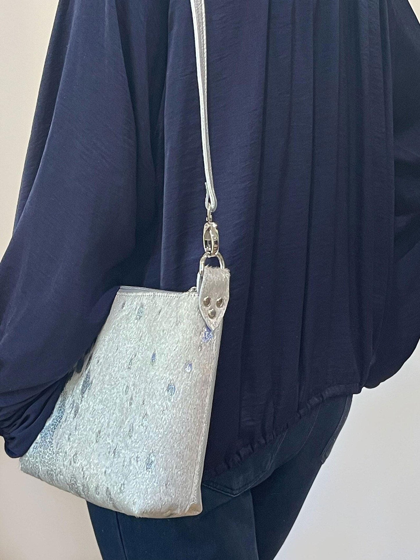 Person wearing a sparkly silver holo acid washed white cowhide crossbody bag with a plain background