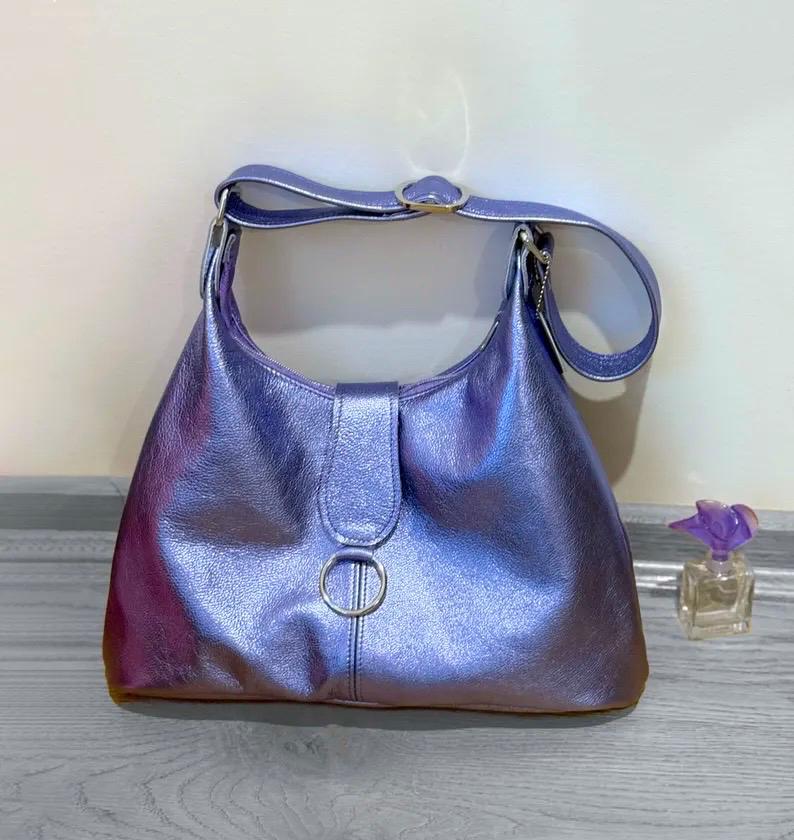 Shiny lavender purple handbag with O ring feature on a wooden surface with a small bottle of perfume next to it.
