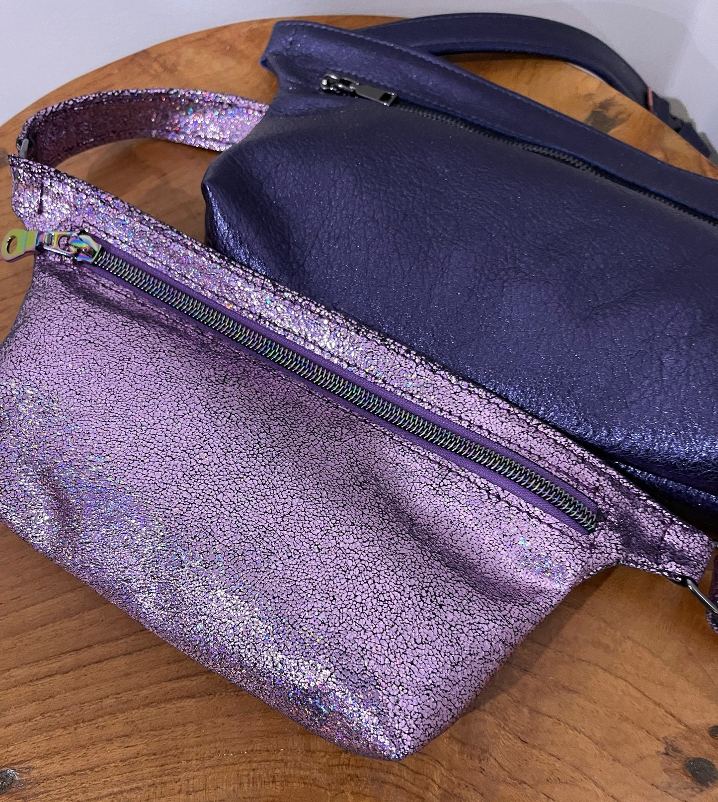 Pink glittery fanny pack bag and navy leather bag on a wooden surface
