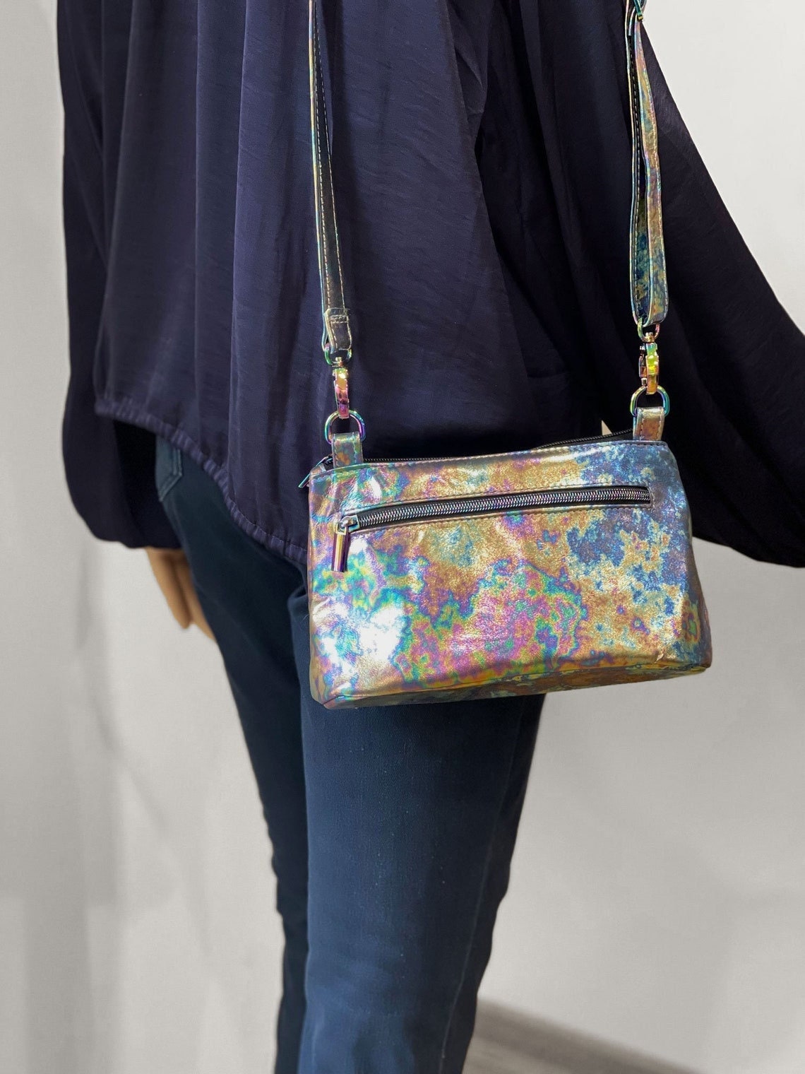 Multicolored tie dye handbag with f lat bottom on models shoulder wearing a dark jacket and jeans