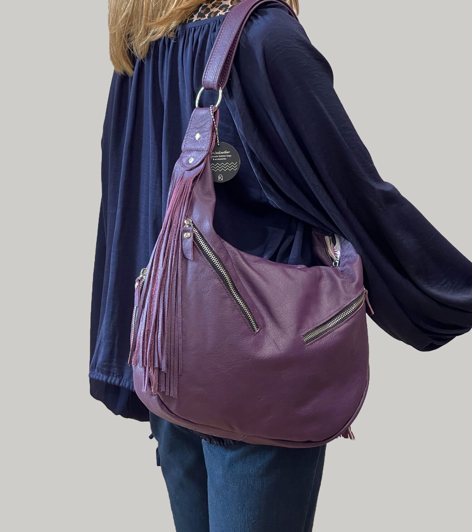 Person wearing a purple Hobo handbag with fringe details and zipper pockets