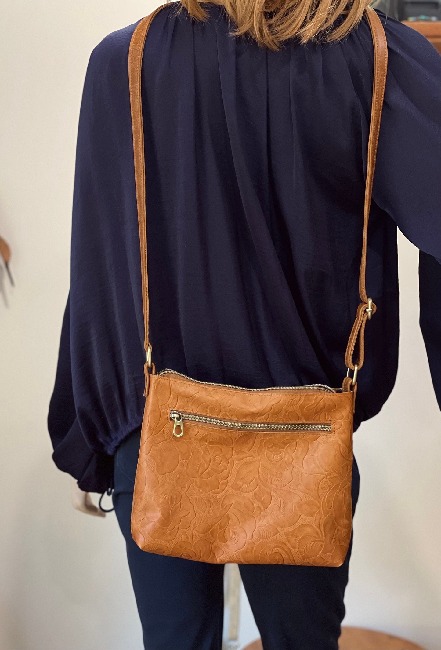 Person wearing a navy blue top with a brown leather handbag over one shoulder.