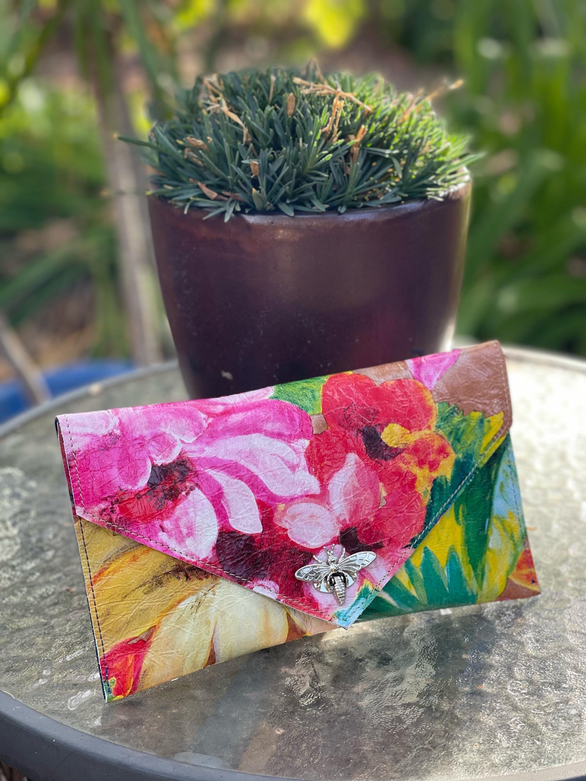 Floral clutch on a reflective surface with a blurred plant in the background