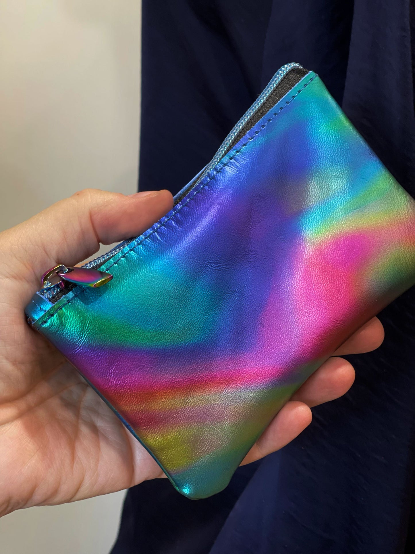 Hand holding a colorful, iridescent pouch with a gradient of blue, green, pink, and yellow.