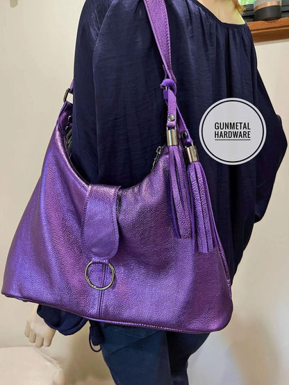 Purple metallic leather handbag with gunmetal hardware held by a person wearing a dark blue top.