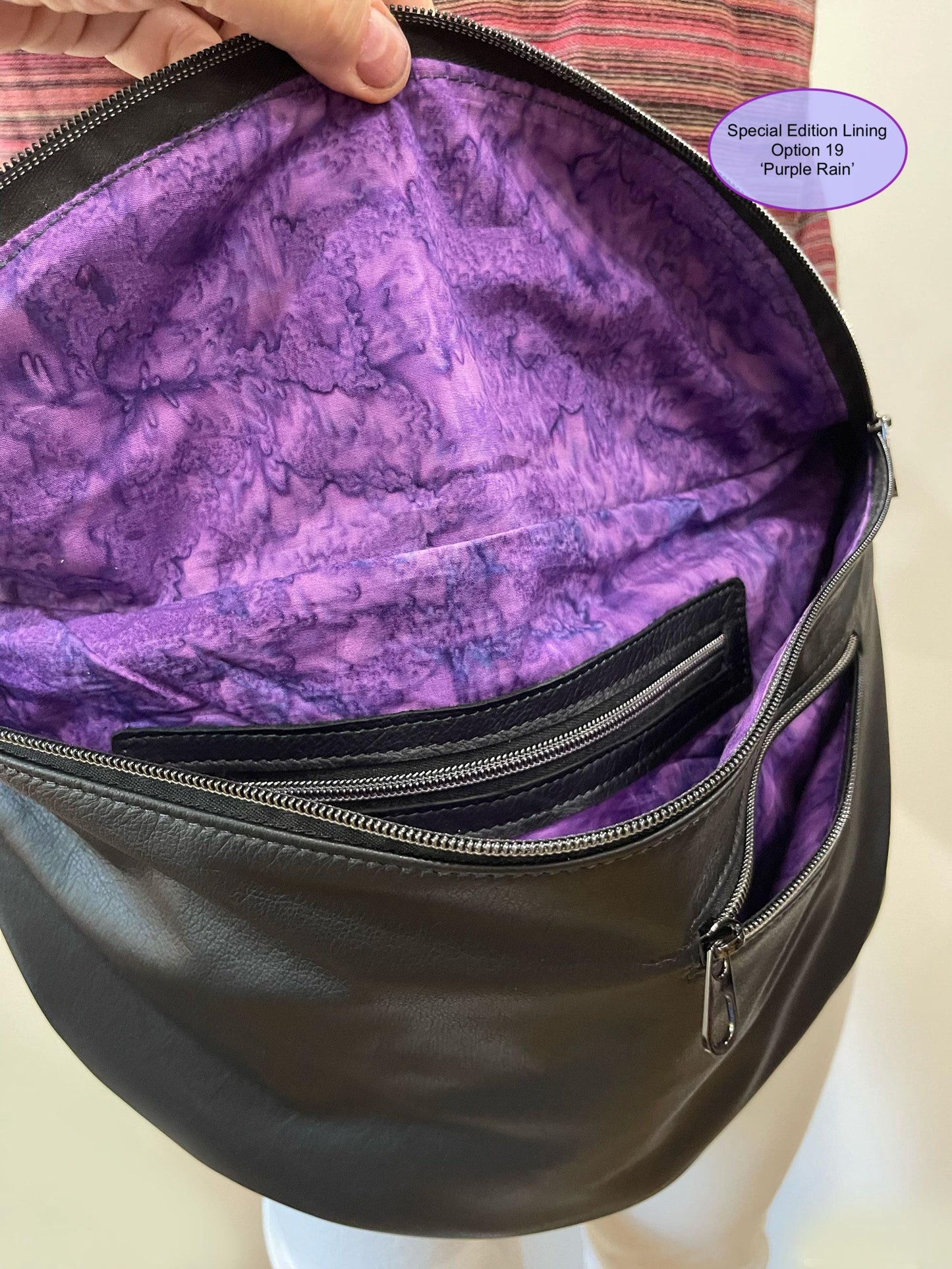 Black bag with purple tie dye lining on a mannequin, labeled 'Special Edition Lining Option 19 Purple Rain'. showing inside and outside  zipper pockets.