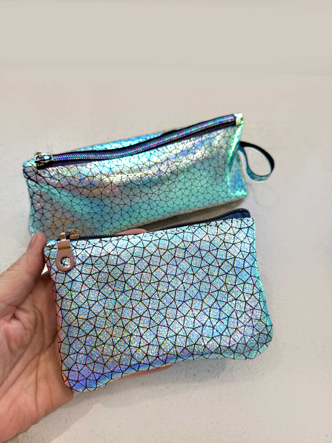Iridescent geometric patterned blue pouch held by a hand on a light background