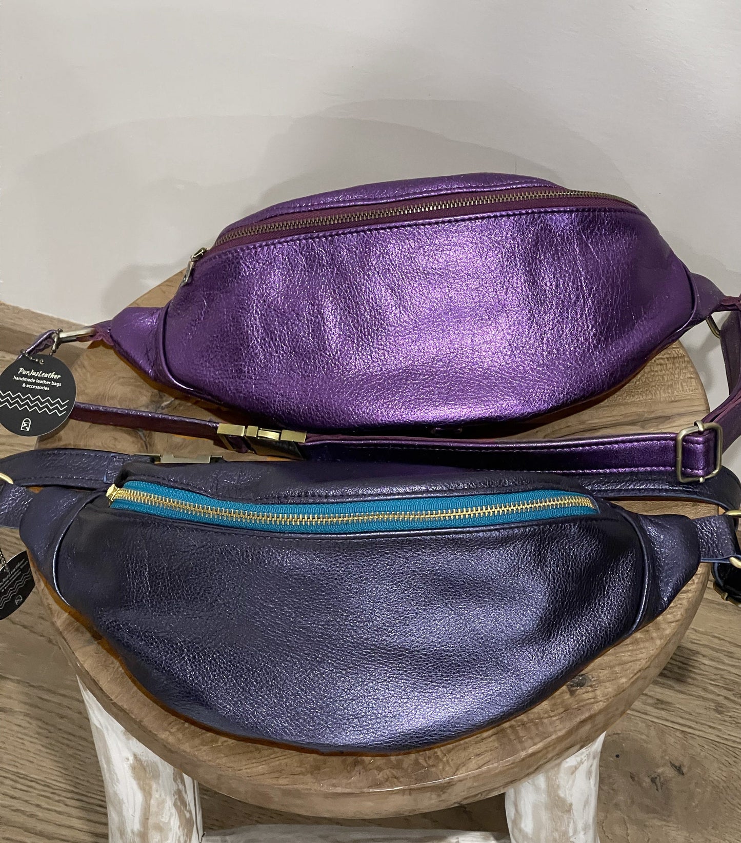Two purple leather waist bags on a wooden stool with a white background