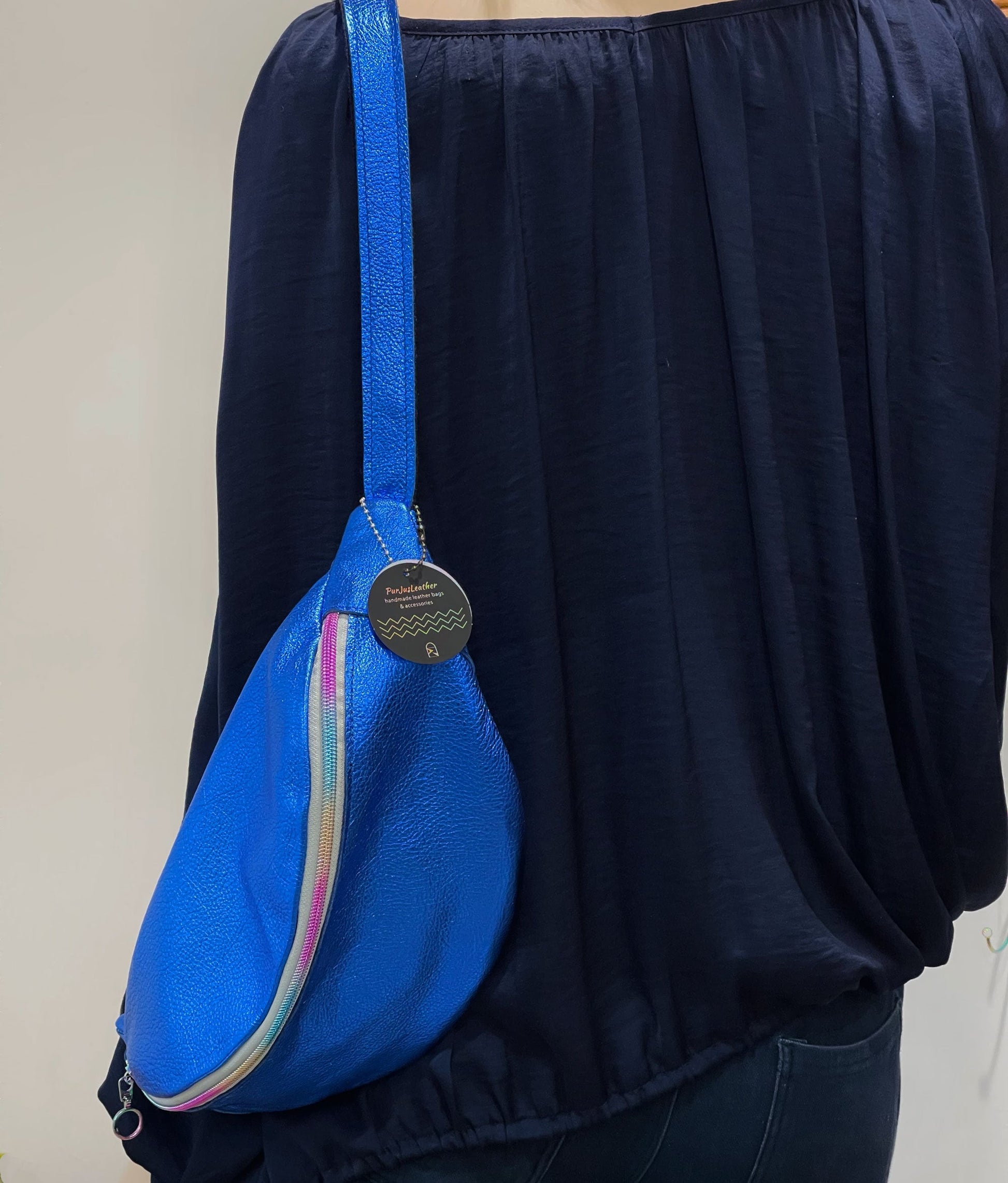 metallic blue crossbody sling bag worn by a person on the shoulder wearing navy