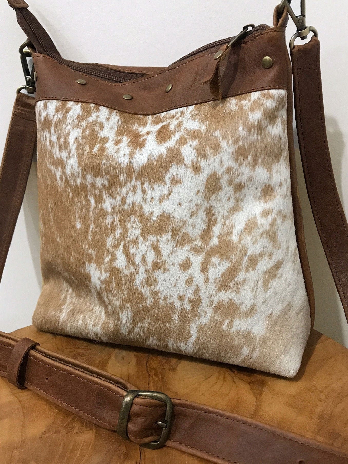 close up of tan and white cowhide leather bag on a wooden surface with a white background
