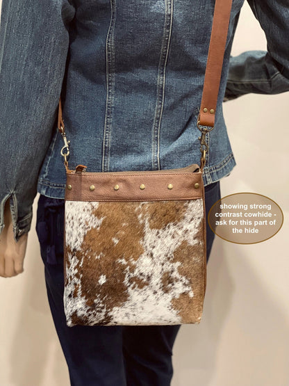 Person wearing a brown and white cowhide crossbody bag with a denim jacket.