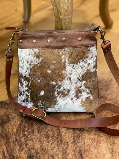 Brown and white cowhide leather crossbody bag showing strong leather adjustable removable leather strap on a wooden surface