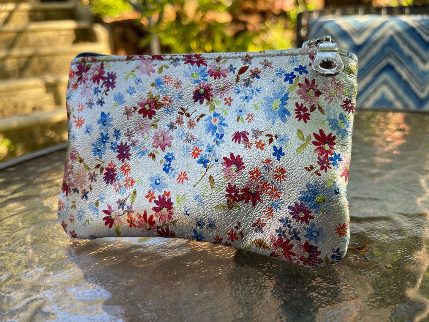 Floral-small colourful ditsy on metallic silver patterned pouch on a reflective surface 