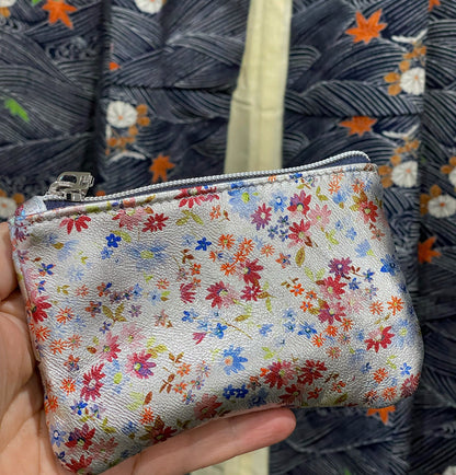 close up of Small floral-patterned pouch held in front of a textured fabric background