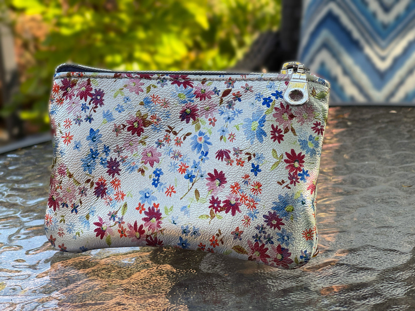 Floral-patterned pouch on a reflective surface with blurred background