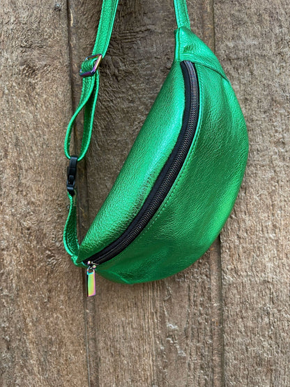 Green leather waist bag with a black zipper on a wooden surface