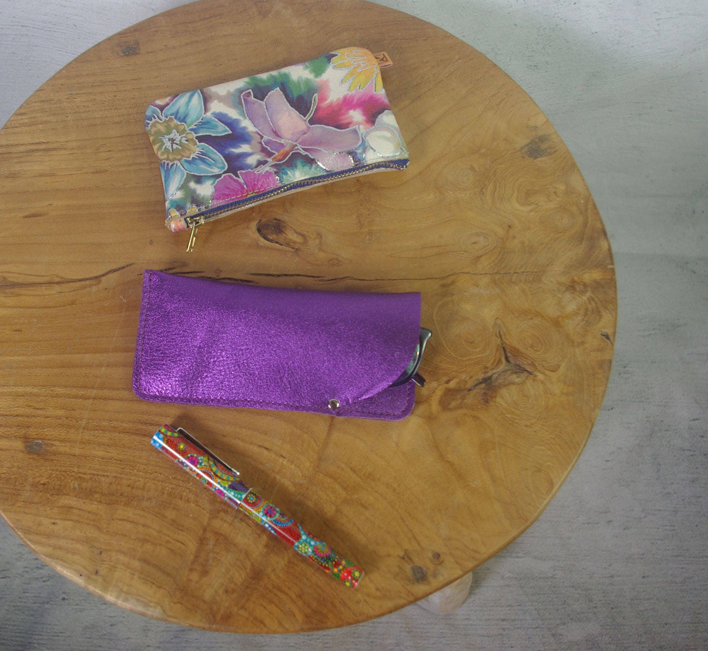 Floral pouch, purple pouch, and colorful pen on a wooden table.