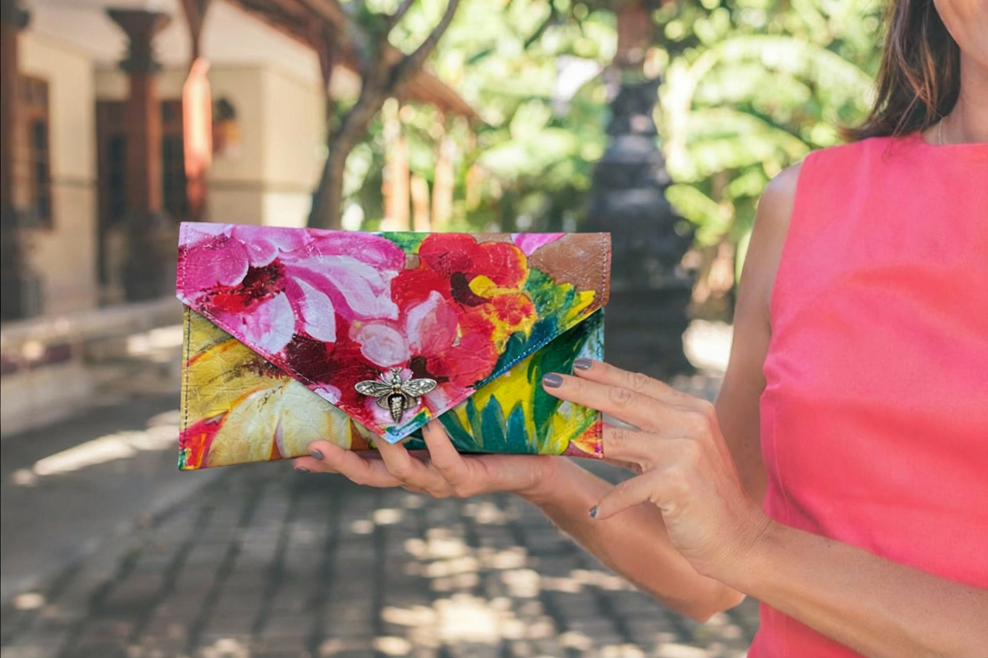 Woman holding a colorful floral clutch with silver metal bee clasp closure, in an outdoor summery setting. great for a wedding or lunch out with friends
