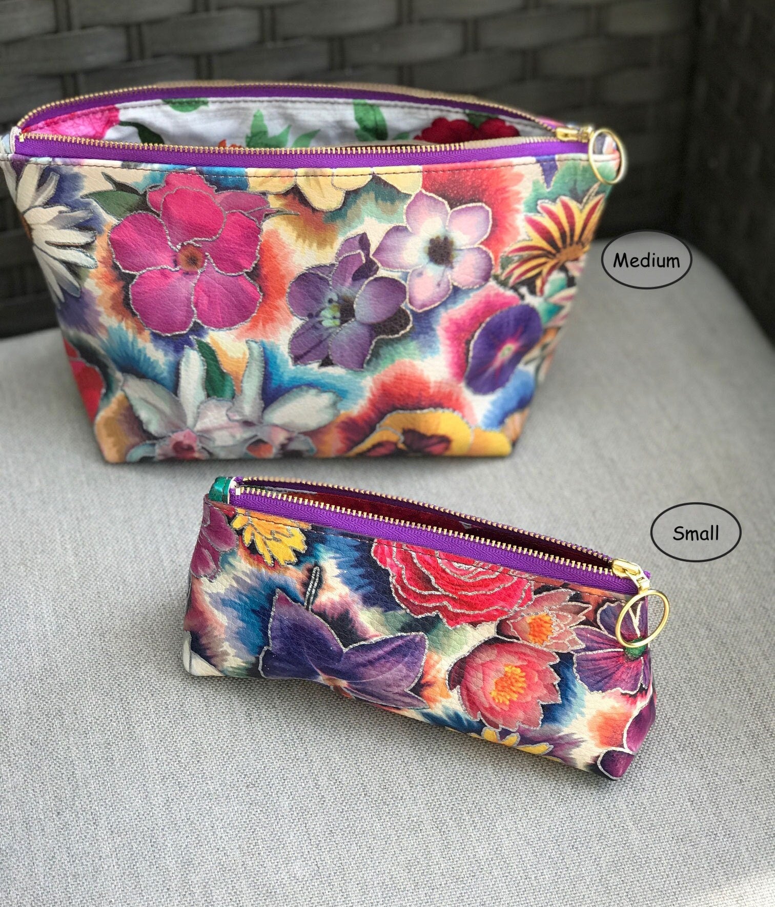 Two tie dye and scrapbook style floral pouches, one medium and one small, on a gray surface with a brick wall background.