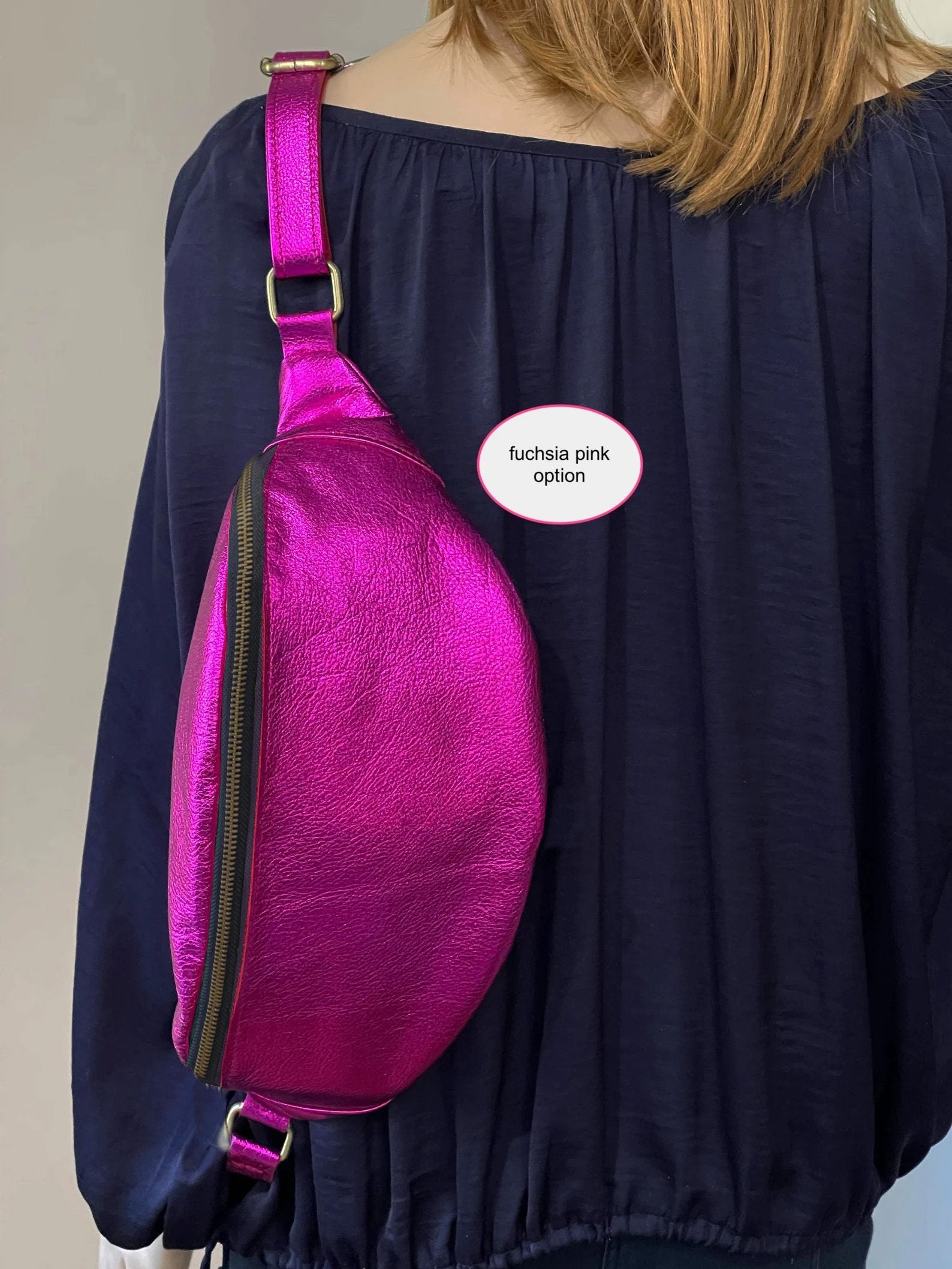 Person wearing a fuchsia pink sling bag with metal zipper close.