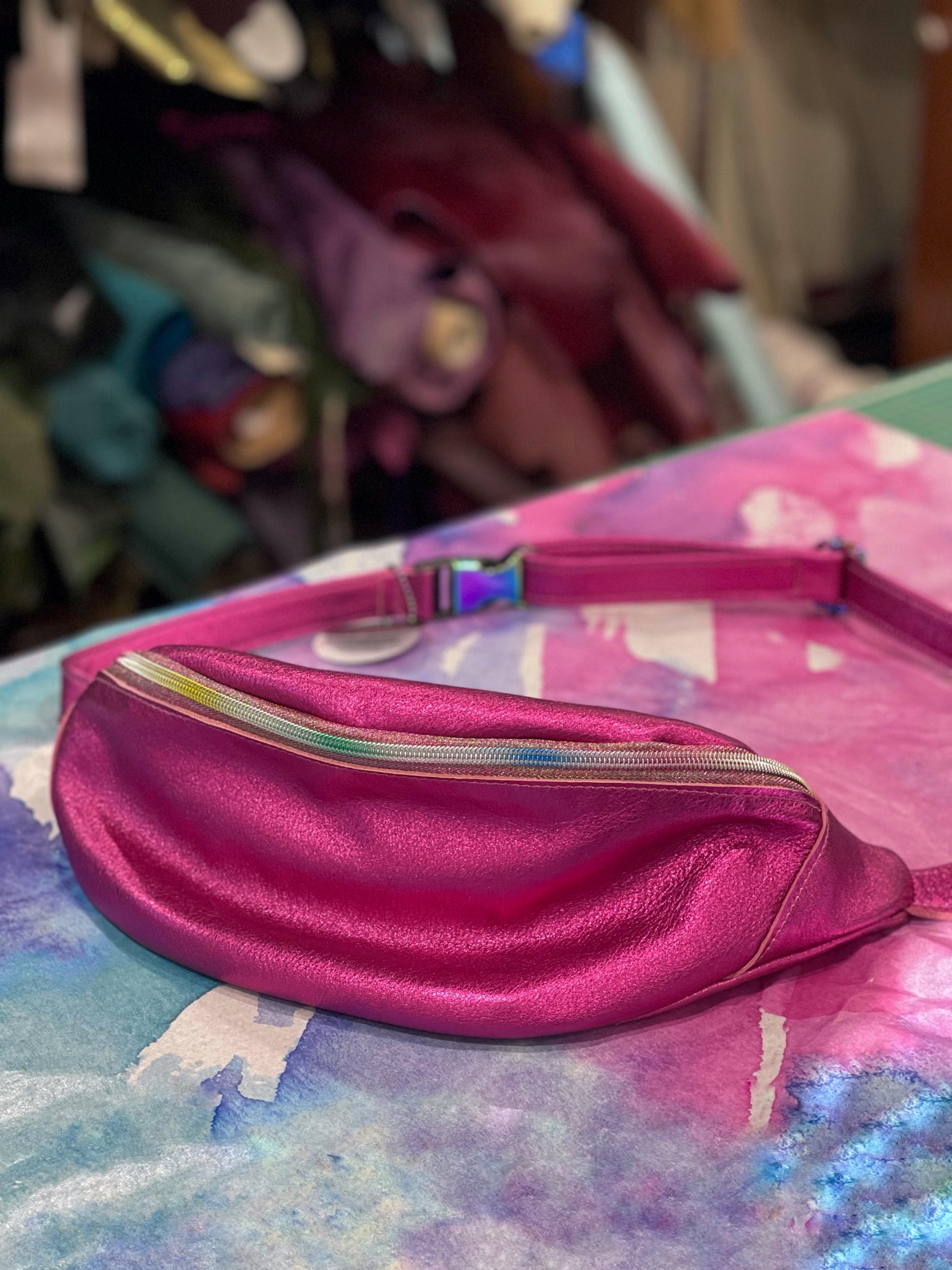 metallic Pink leather fanny pack with rainbow zipper on a colorful surface with a blurred background