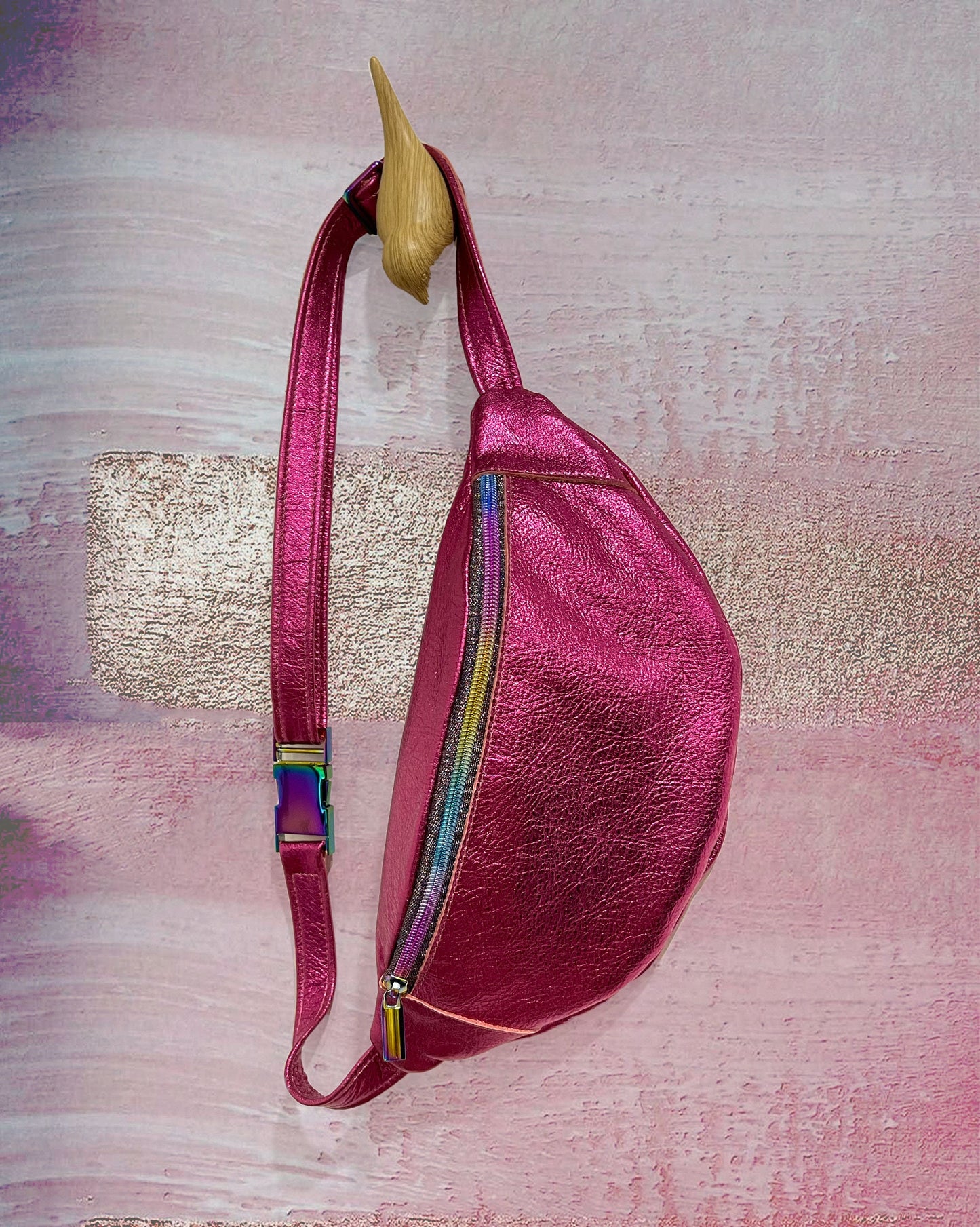 Pink leather sling bag with colorful zipper on a textured pink background