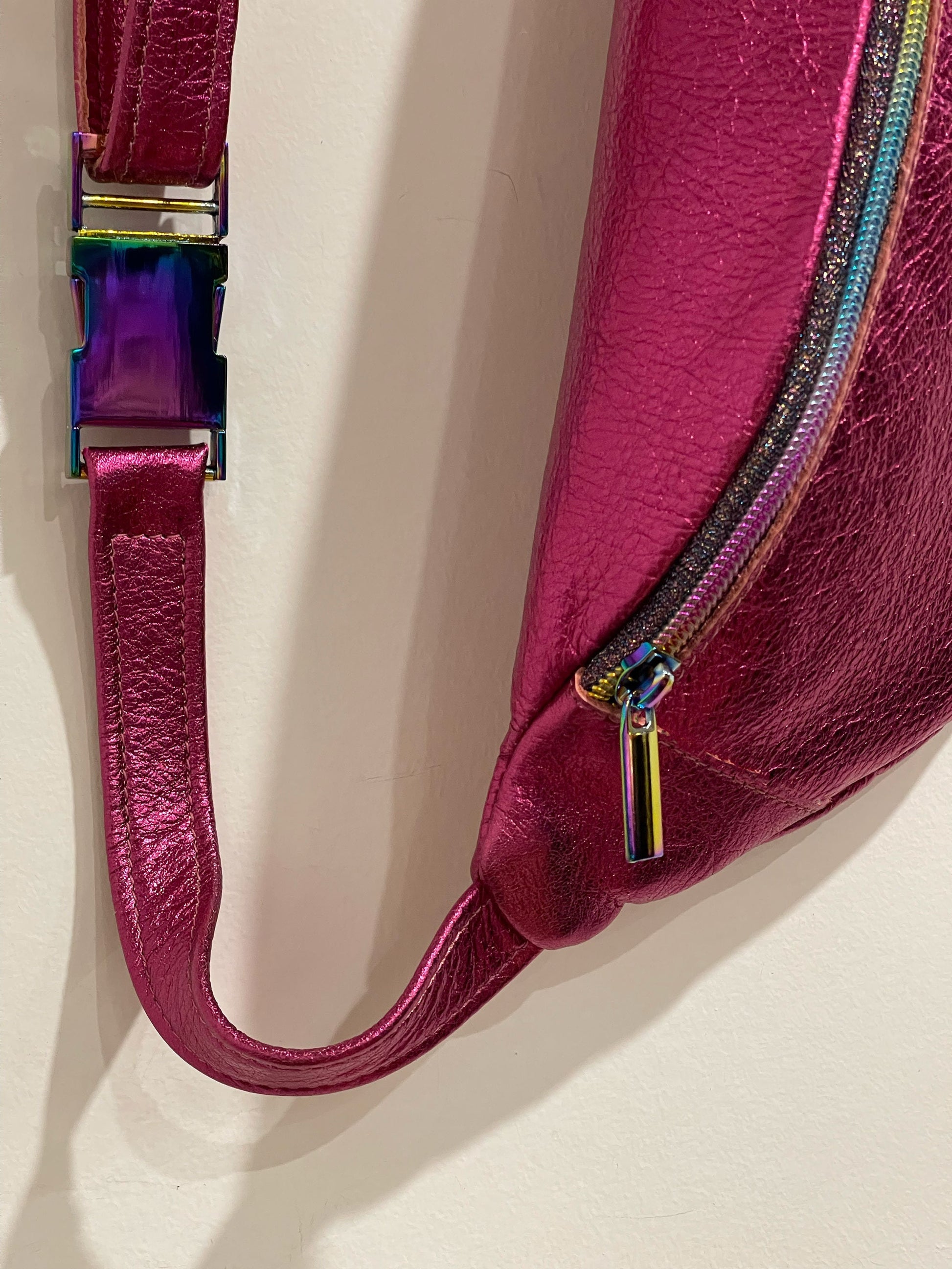 Close-up of metallic pink leather fanny pack with a colorful zipper pull on a light background